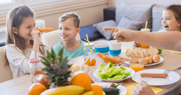 Kids at dinner table. Girl using a carrot as a nose.