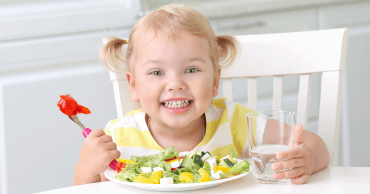 Toddler girl happily eating salad