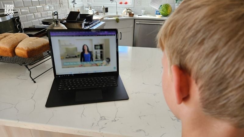 person watching video lesson on laptop in kitchen