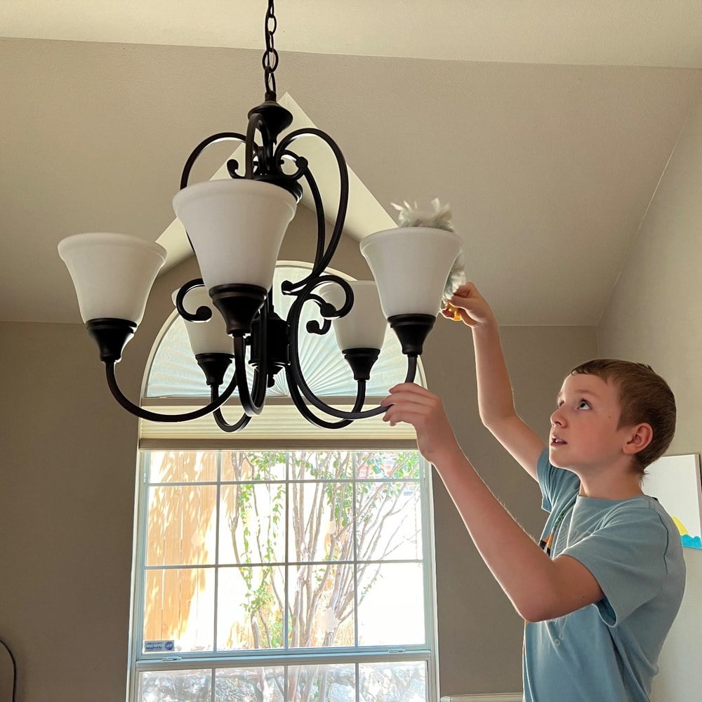 A boy reaching up to dust the chandelier above the stairs