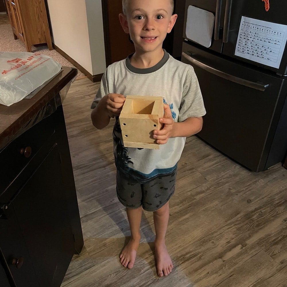 A young boy holding the wooden pencil holder he built