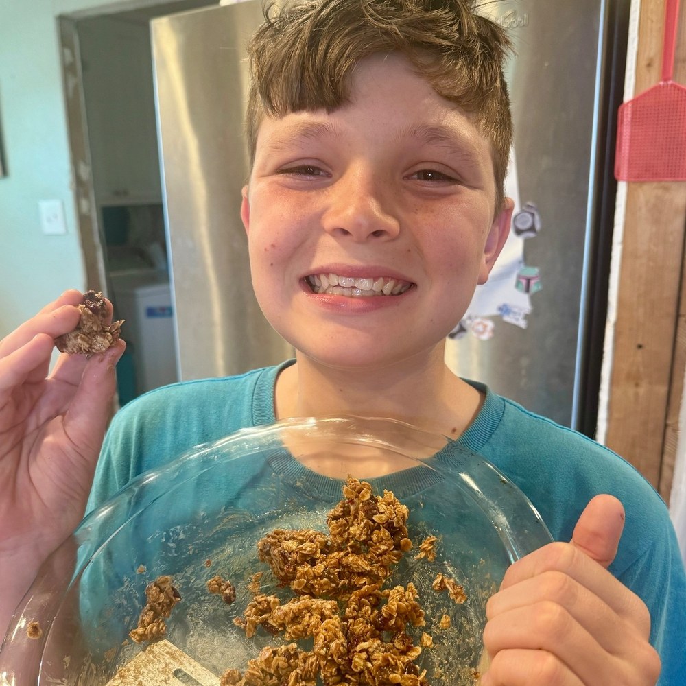A boy giving a thumbs up over the bowl of granola mixture he made