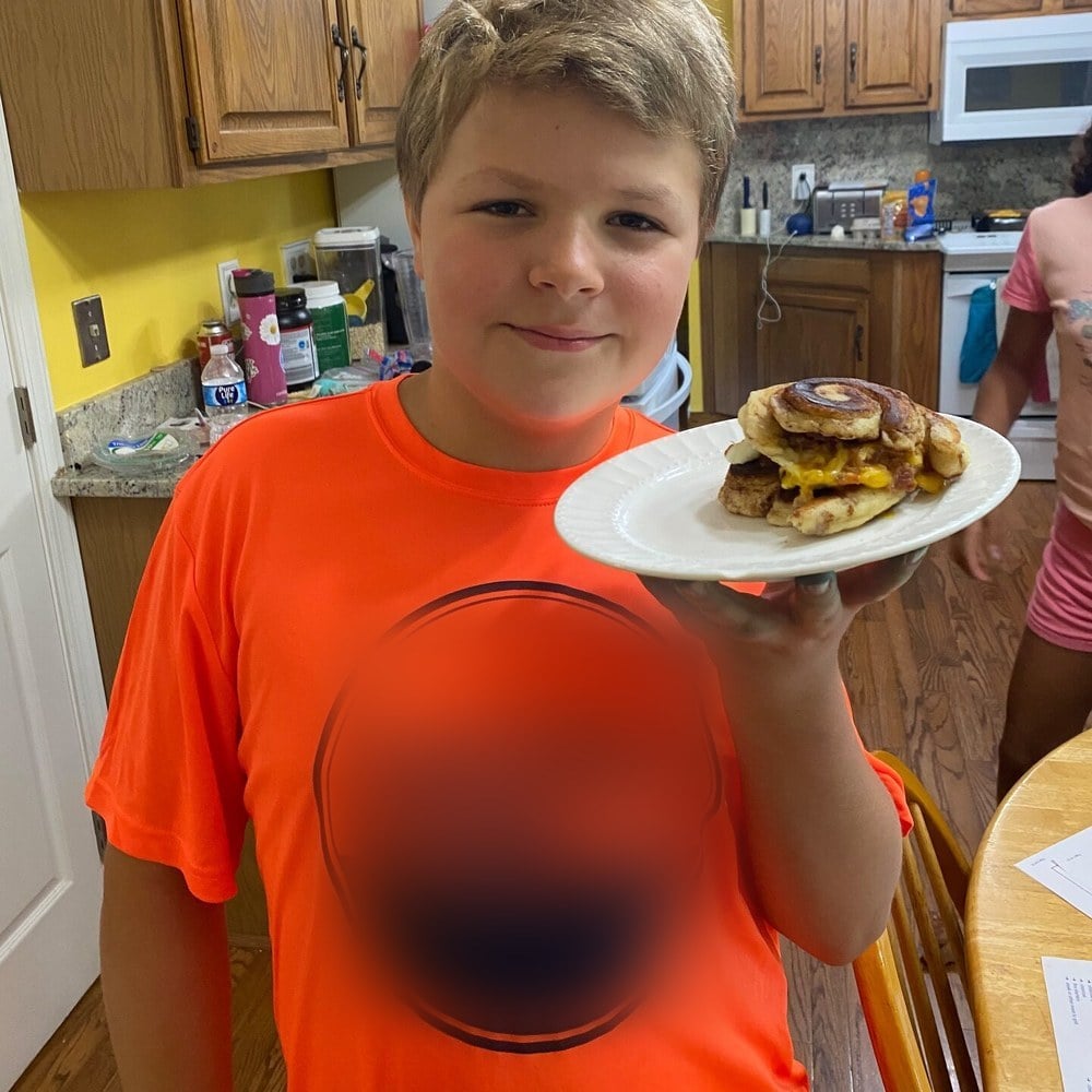 Boy holding the cinnamon roll breakfast sandwich he cooked