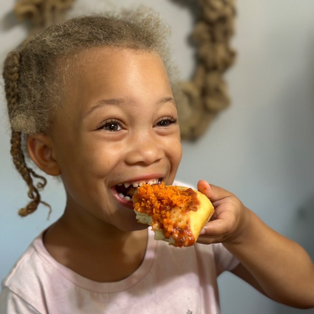 Girl taking a big bite of the veggie pizza she made