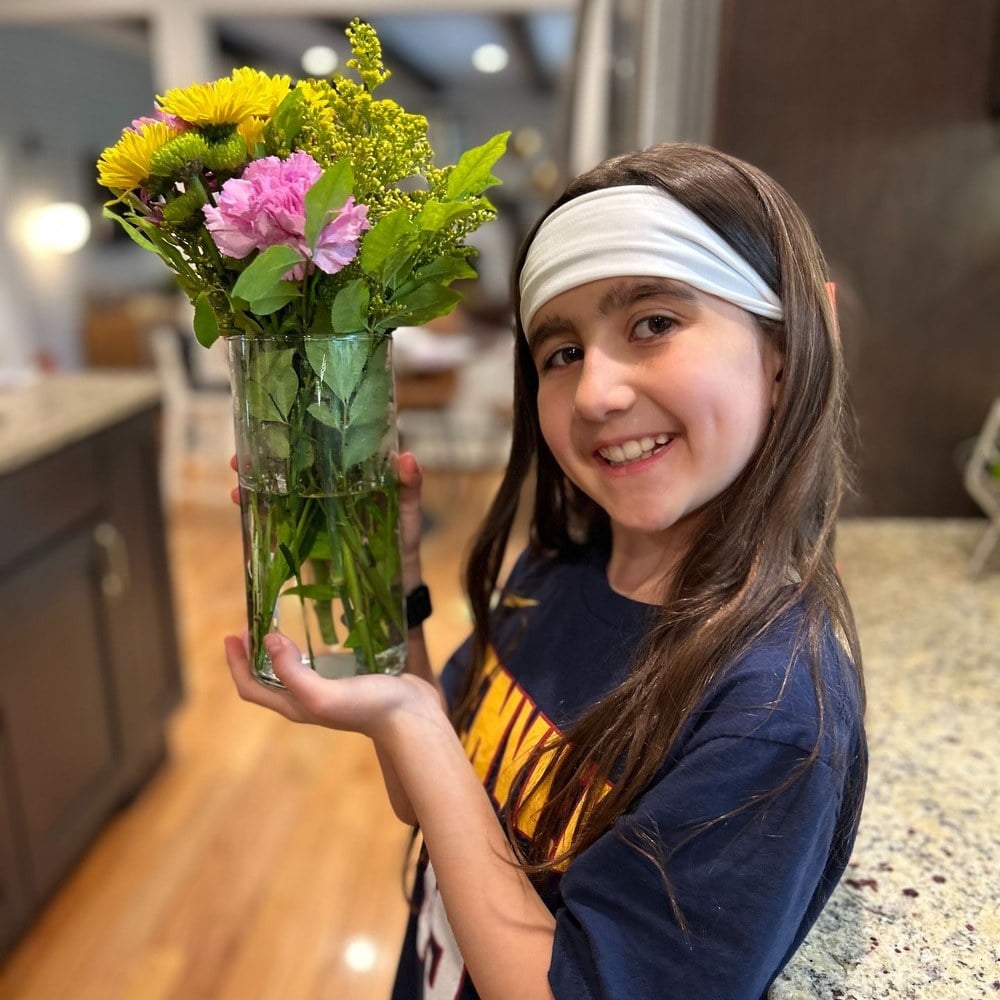 A girl holding the flower bouquet she arranged in a glass vase