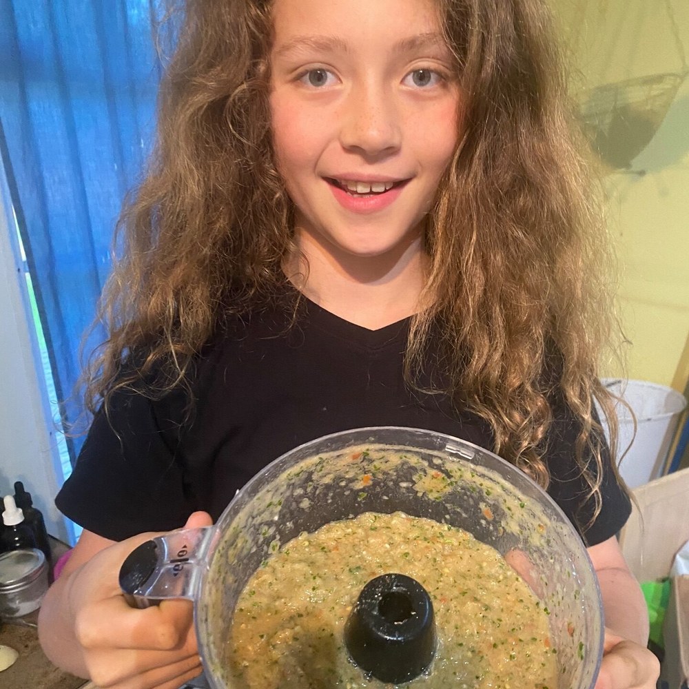 A girl holding up the food processor bowl full of salsa she made