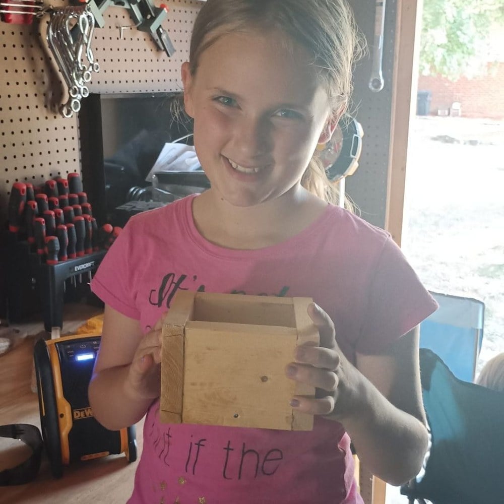 A girl holding up the wooden pencil holder she built
