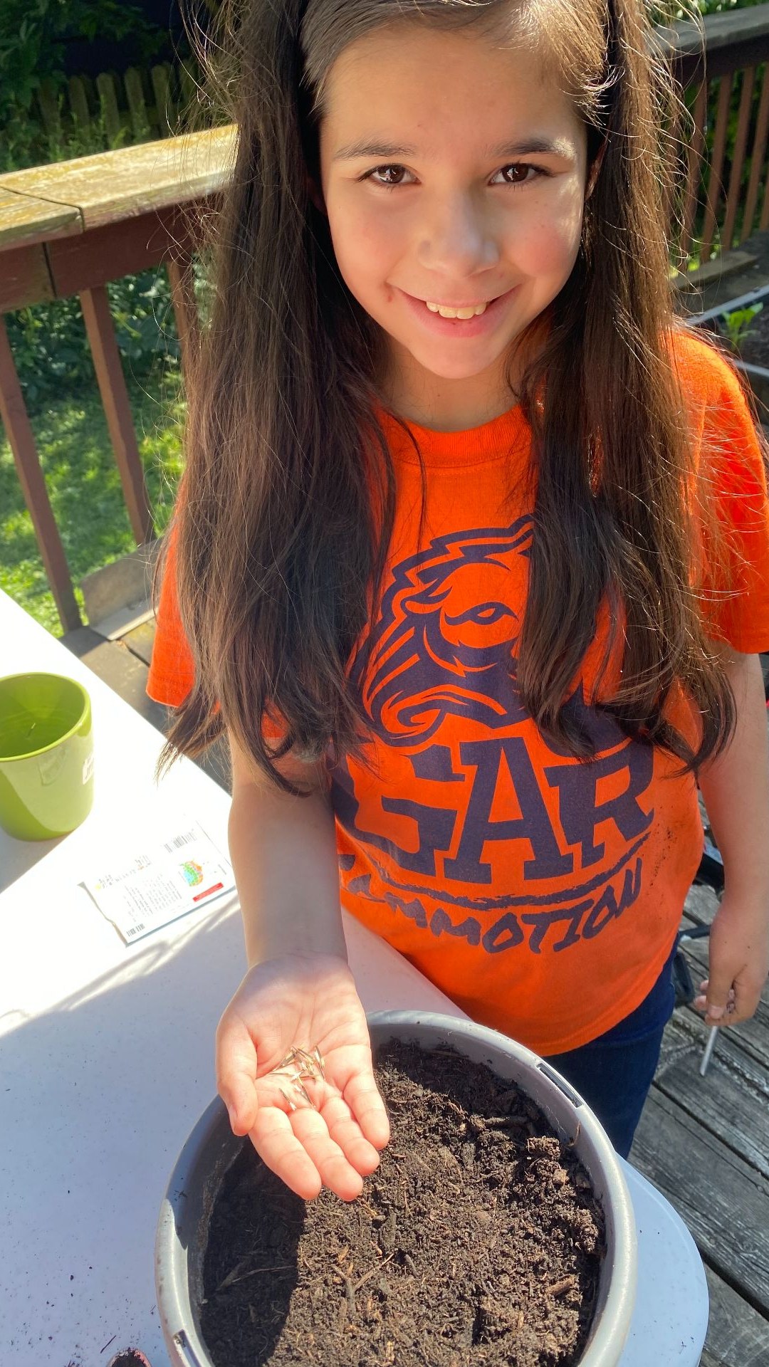 Girl holding a handful of seeds over a pot of soil