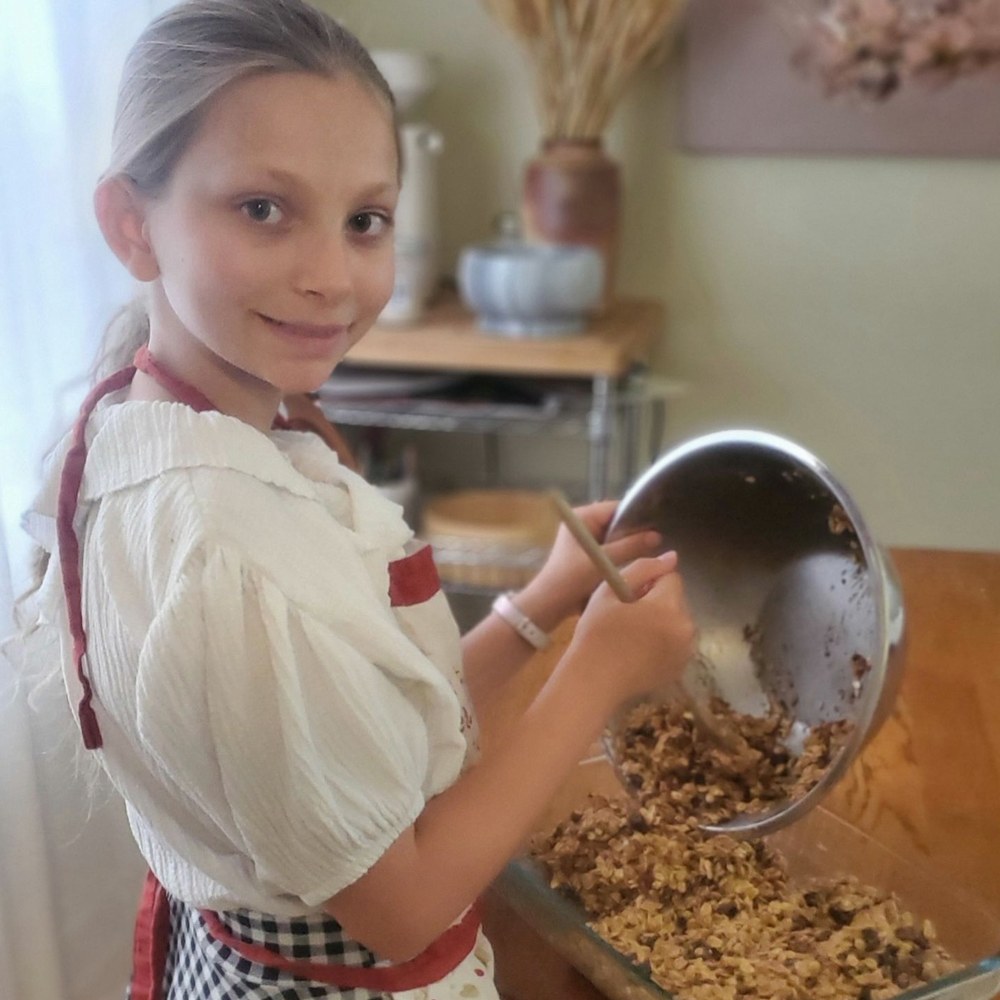A girl in an apron tipping the granola mixture into a glass pan