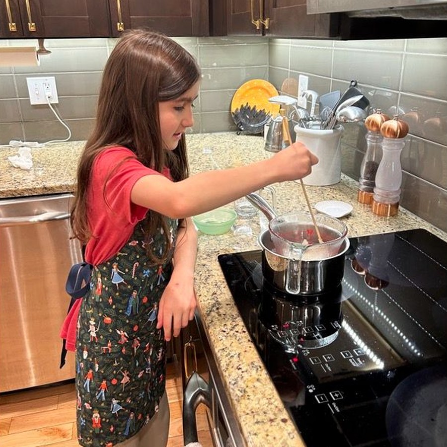 A girl stirring a small pot on the stove, making lip balm