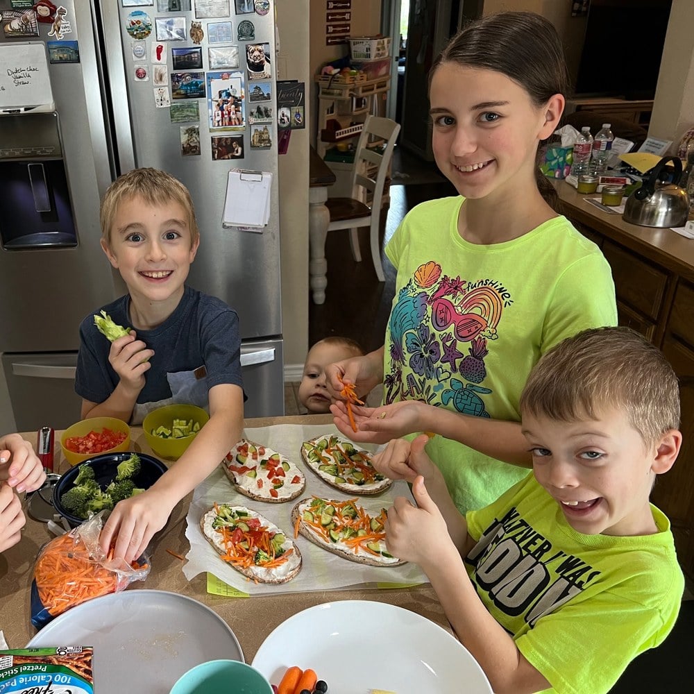 Four children around a table building their own veggie pizzas