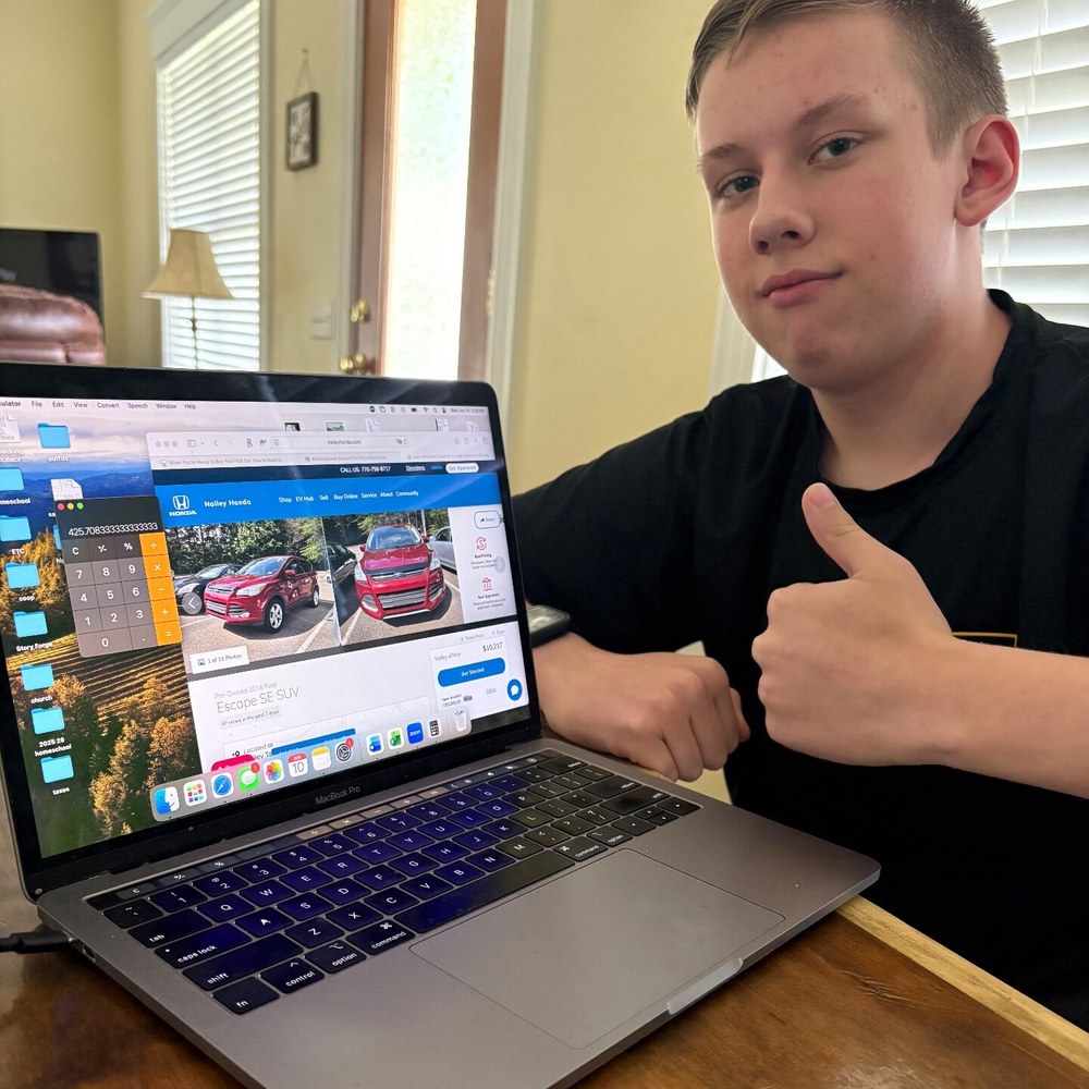 Teenage boy giving a thumbs-up over his laptop while car shopping