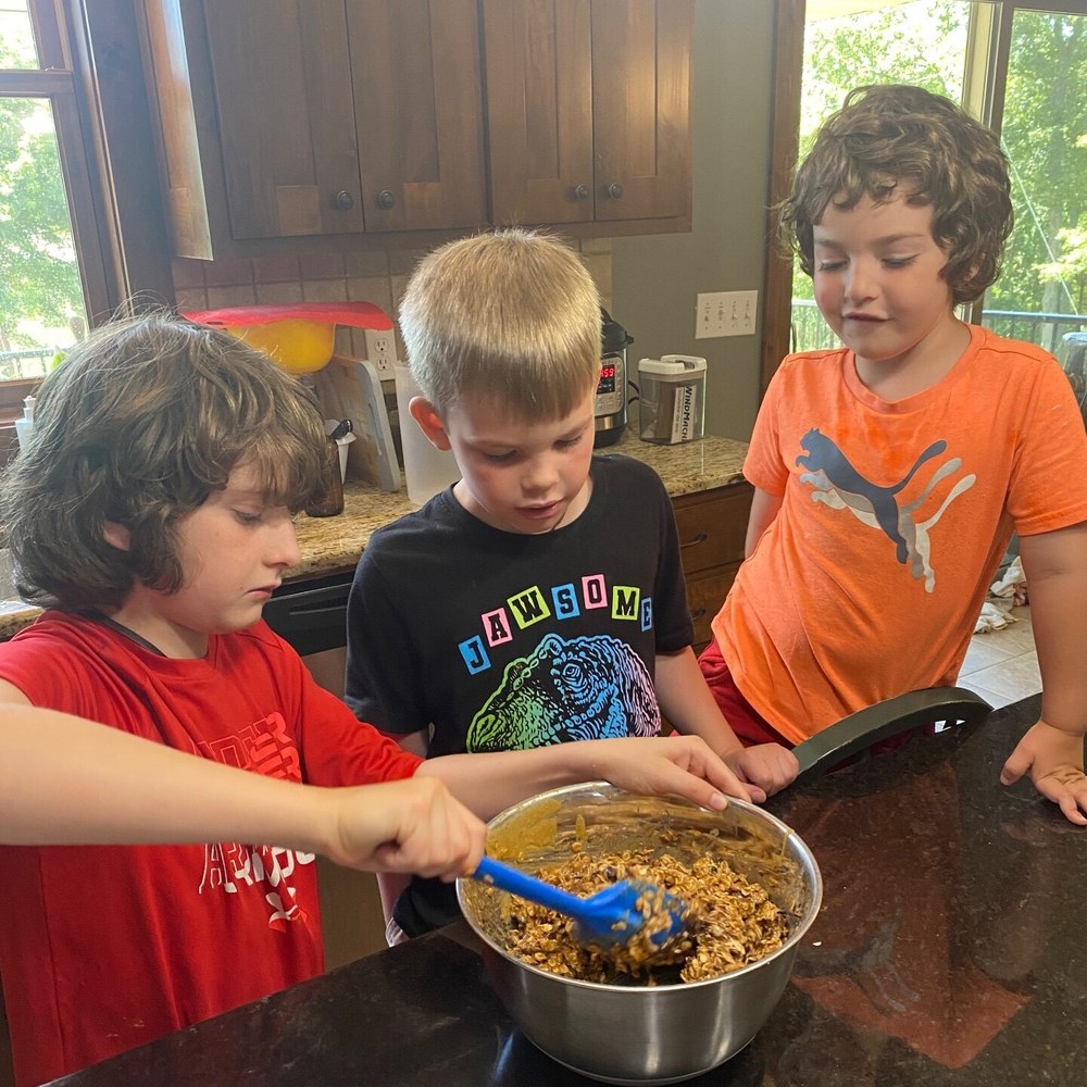 Three boys around a mixing bowl at the kitchen counter, one stirring
