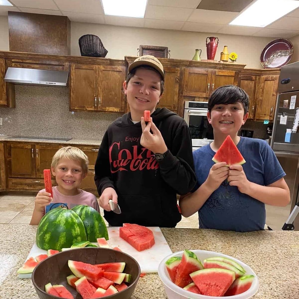 Three children in the kitchen with the watermelon they cut up
