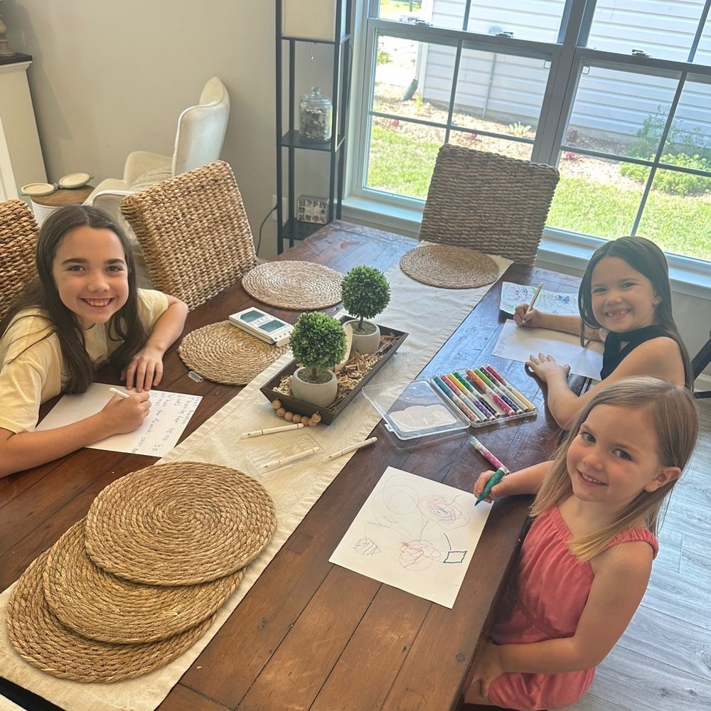 Three children writing letters together at the dining table