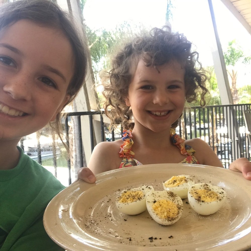 Two girls holding out a plate of the hard cooked eggs they made