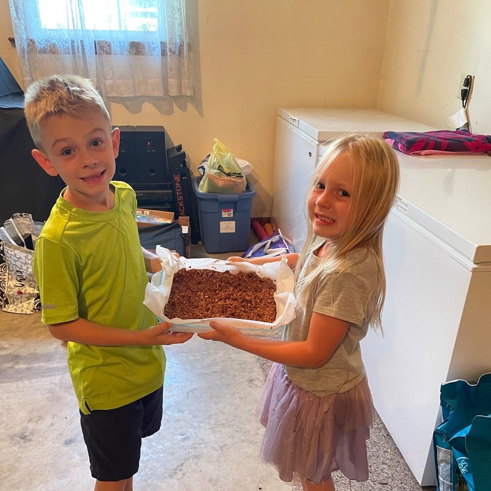 A boy and a girl carrying a tray of granola bars between them
