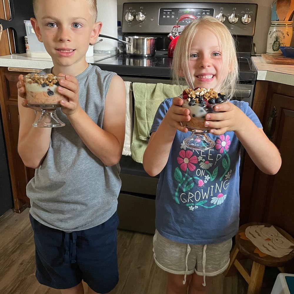 A boy and a girl each holding a parfait glass of the snack they made