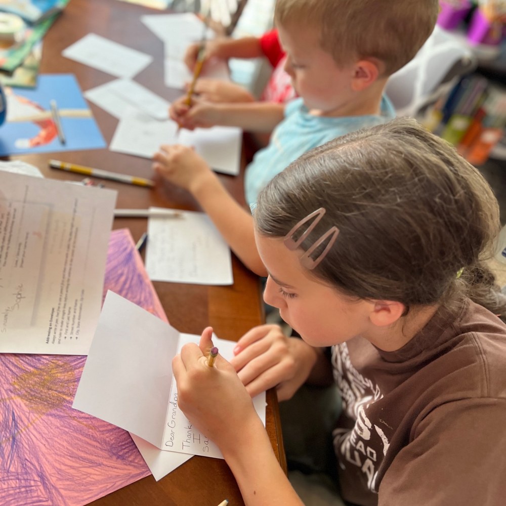 Two children writing thank-you cards at the dining table