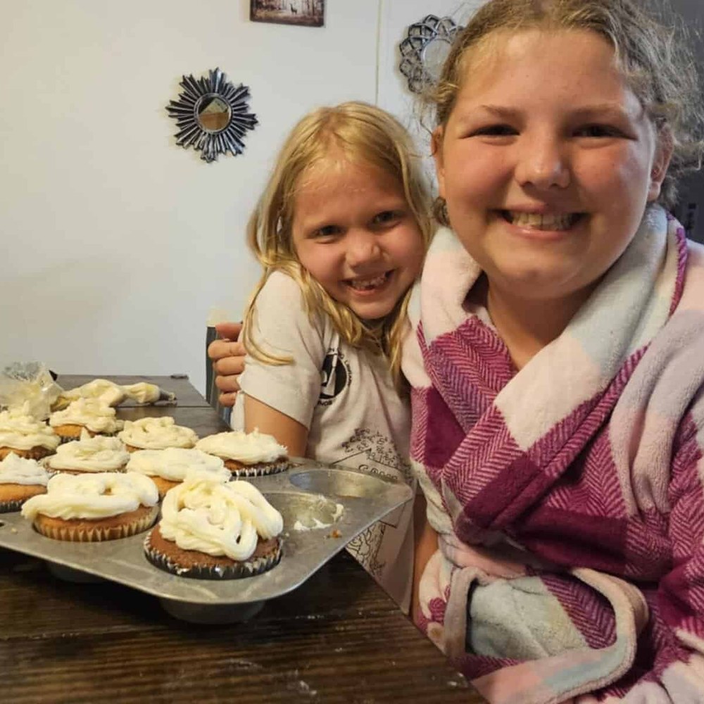 Two sisters smiling behind a tray of cupcakes they frosted